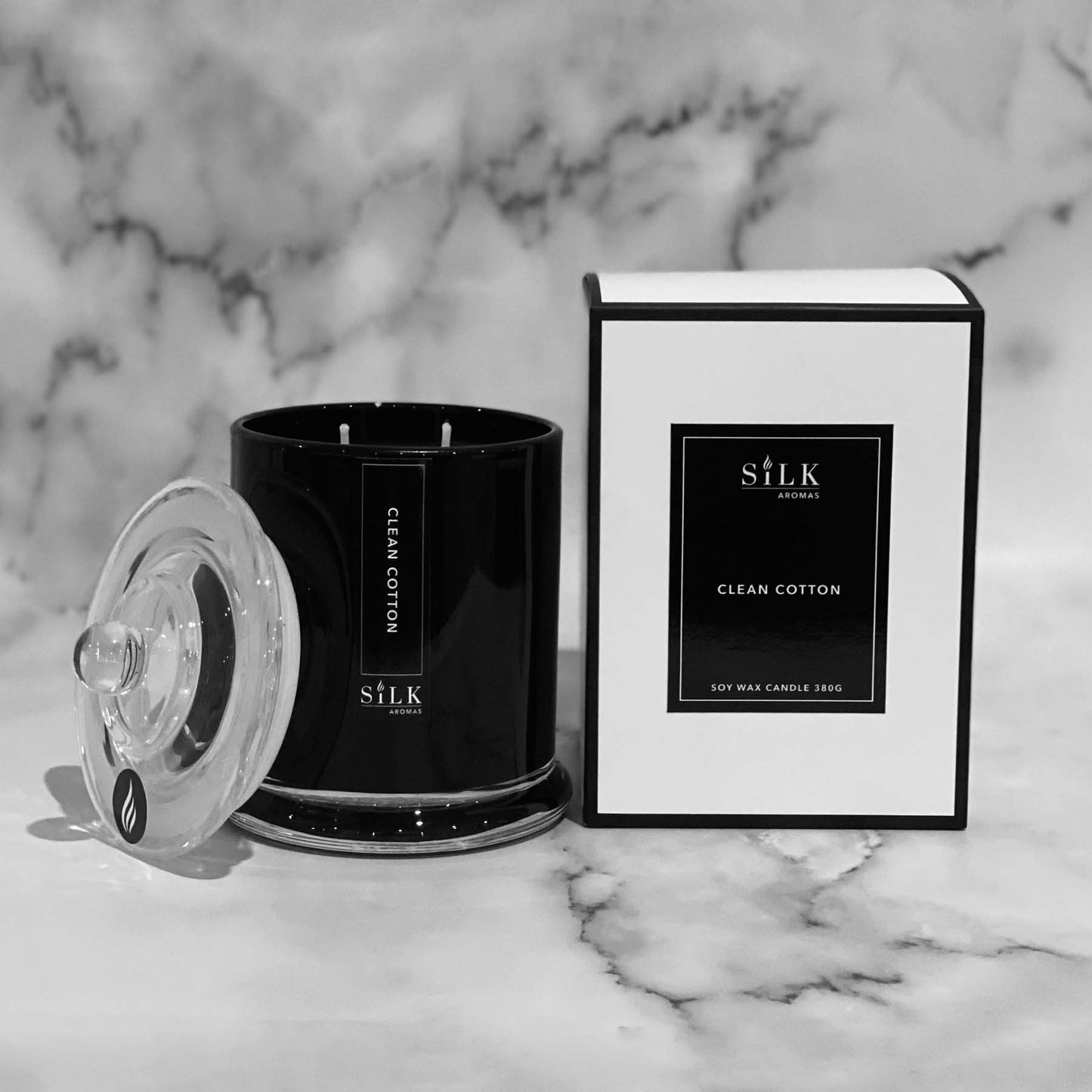 A black glossy candle jar with clear glass apothecary lid, next to a luxury white box with a black label and black trim