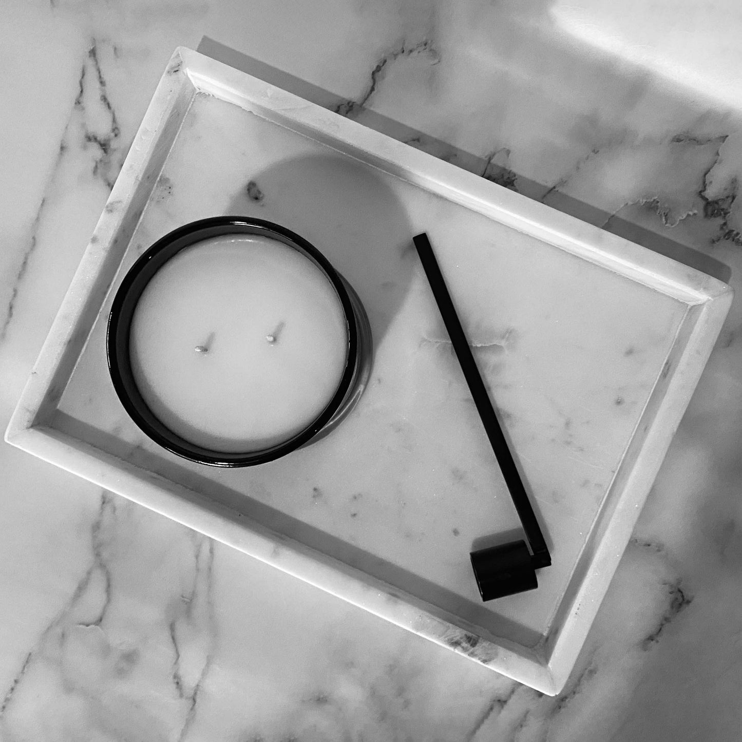 A sleek, black candle snuffer on a white marble tray