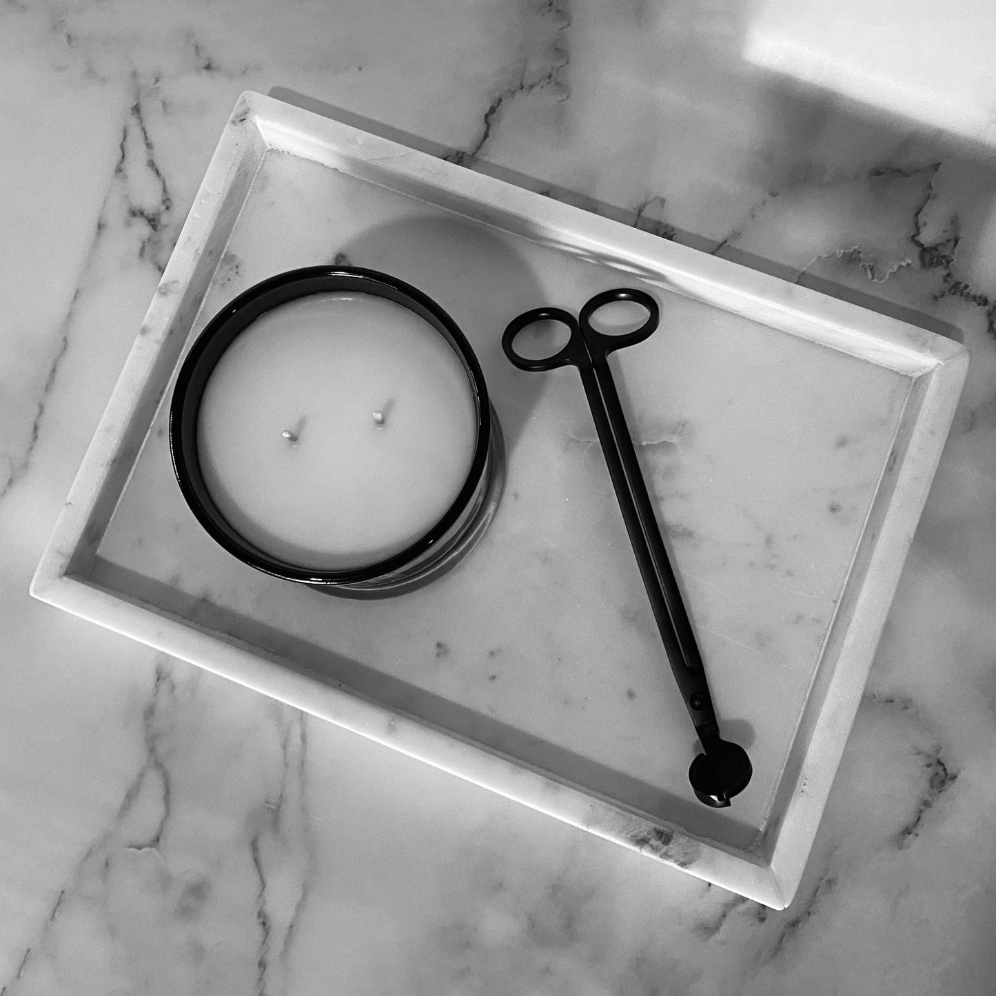 A sleek, black wick trimmer on a white marble tray